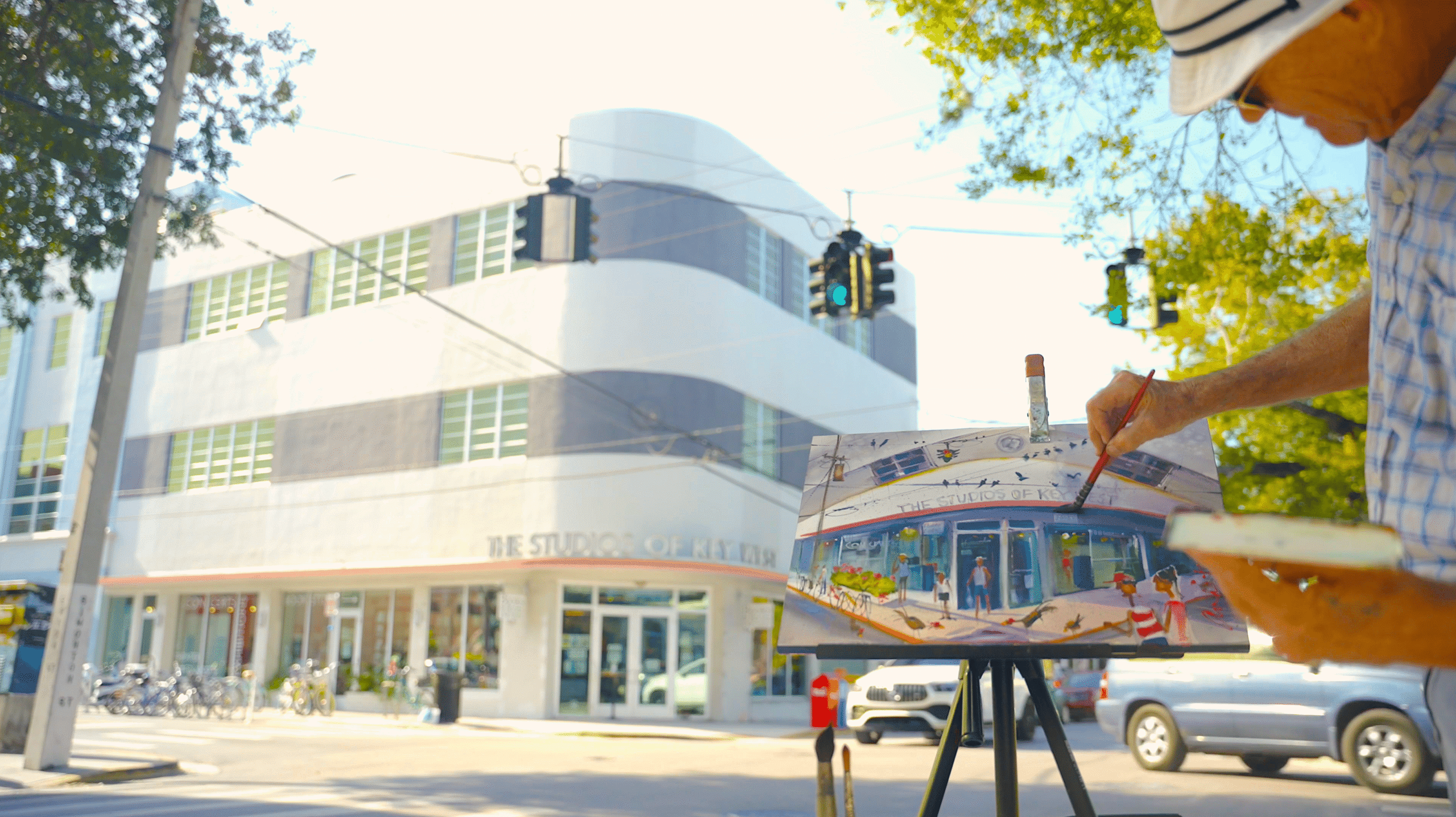 A photo of the Studios of Key West iconic, curved building with an artist in the foreground paining a picture on an easel.