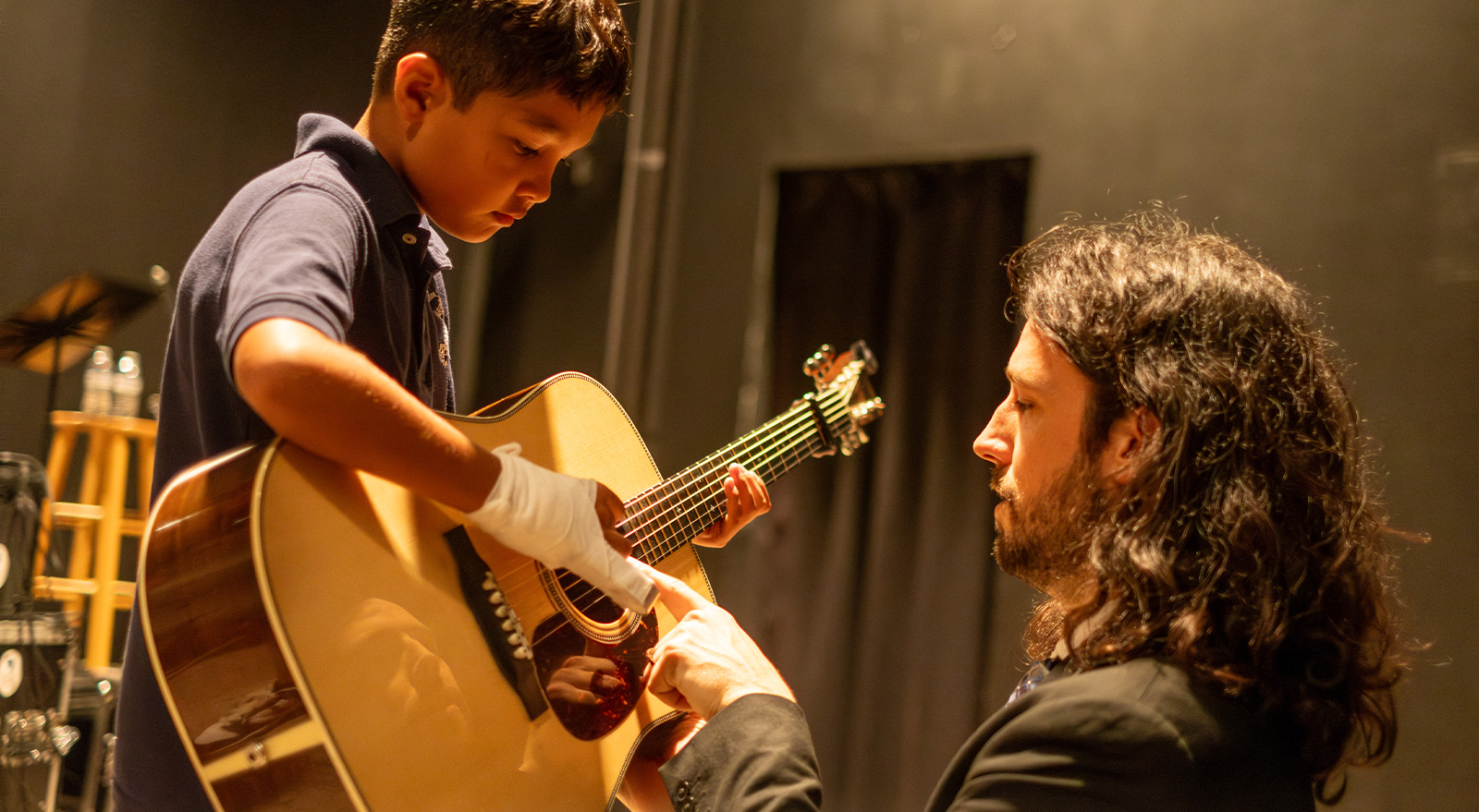 A musician helps a young student play an acoustic guitar during a youth music program at The Studios of Key West.