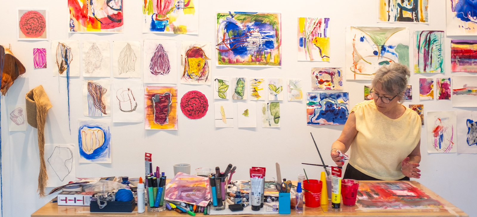 Artist Jan Blythe works at a table surrounded by colorful drawings and paintings during her residency at the PEAR House.