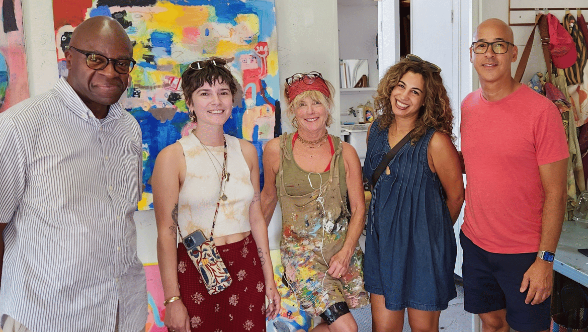 Five people smiling together in a working studio, standing in front of a large colorful abstract painting.