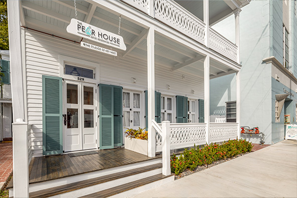 Exterior of the PEAR House, a historic white Key West home with green shutters and a covered front porch.