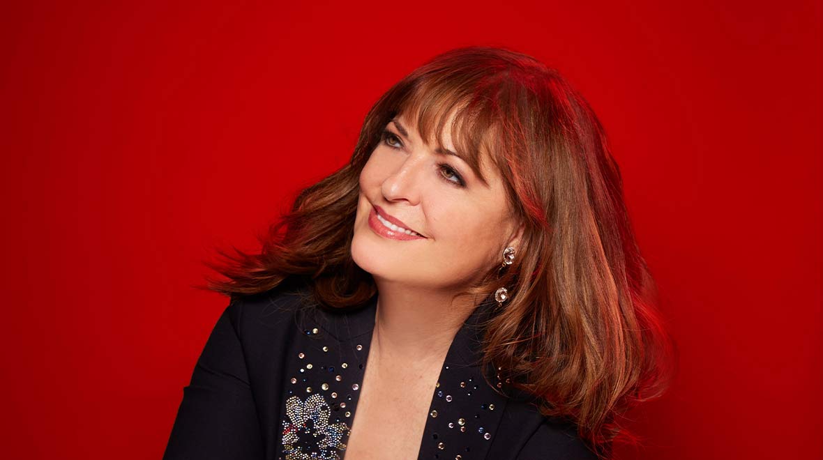 Portrait of Ann Hampton Callaway smiling and looking upward against a vivid red background.