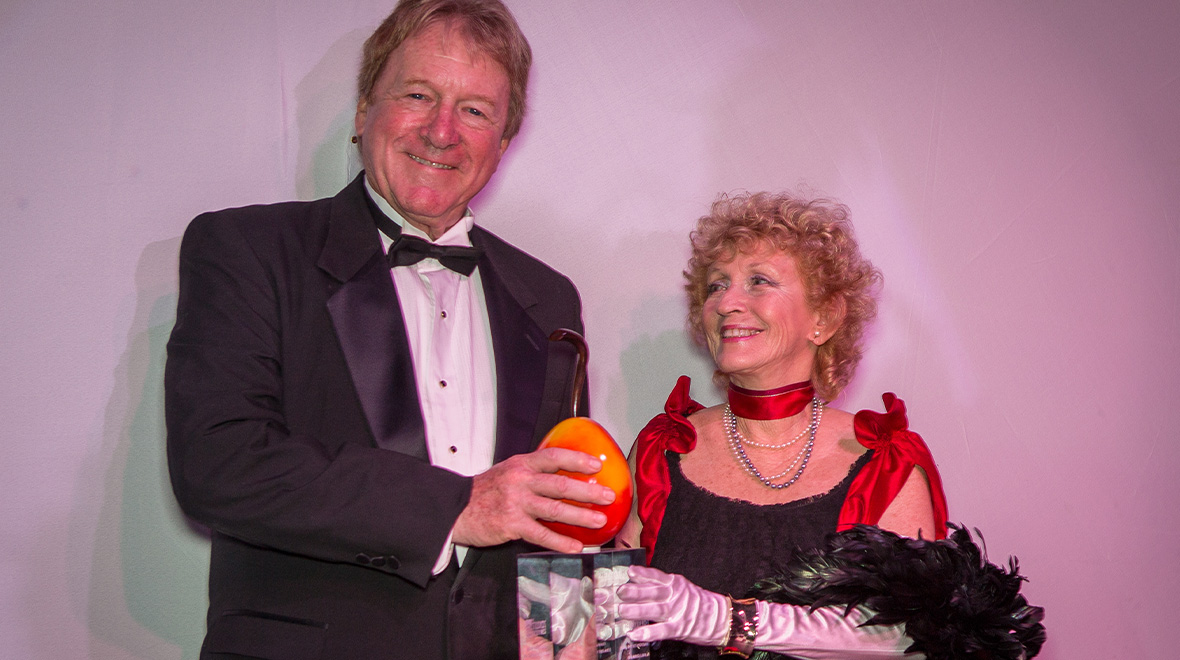 Couple in formal attire smile together as the man holds a Golden Mango Award.