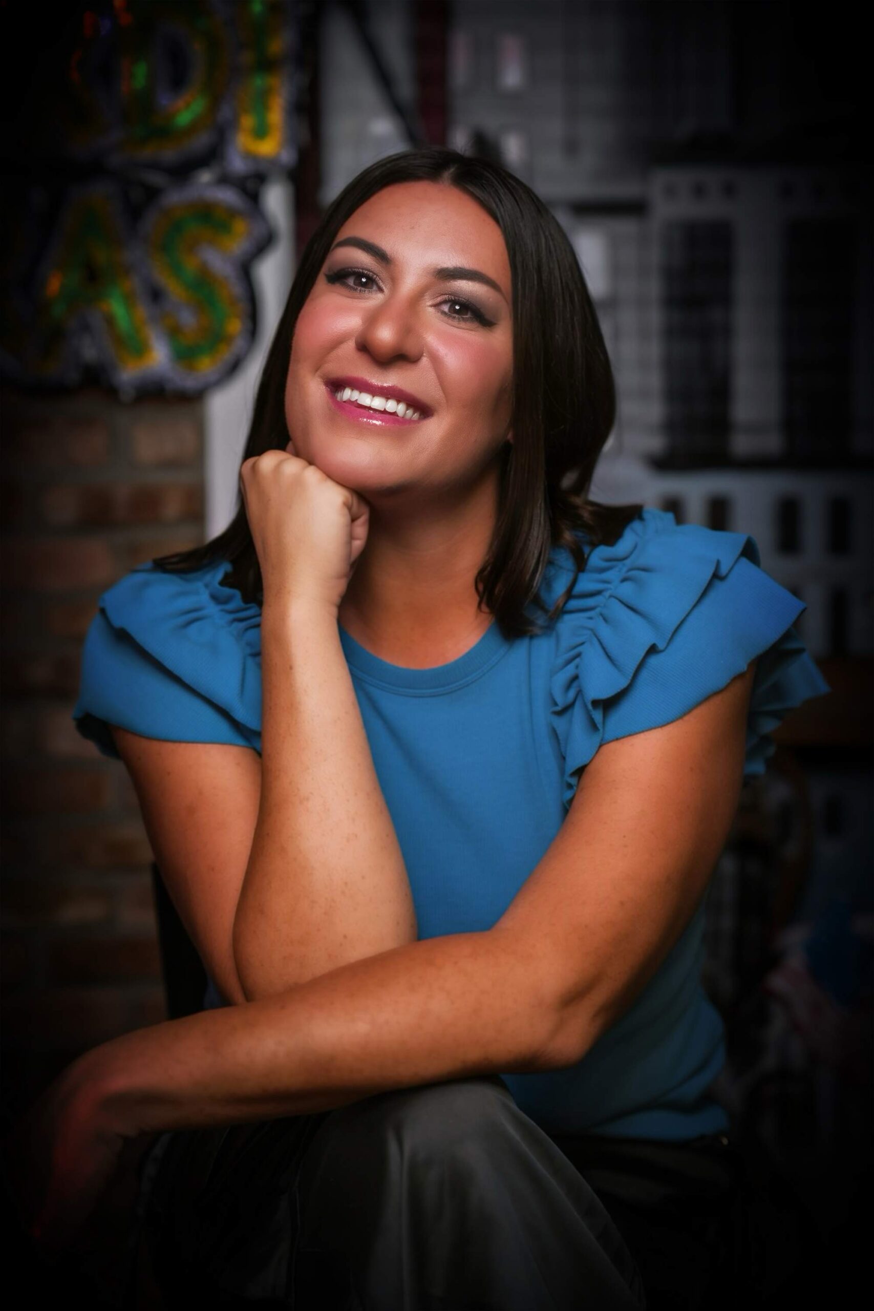 Portrait of Bria smiling in a bright blue top, resting her chin on her hand against a softly blurred background.