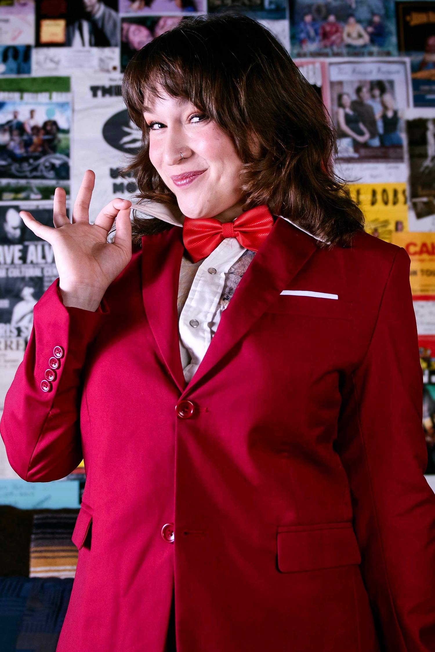 Bryn Battani poses in a bright red suit and bow tie against a wall of posters.