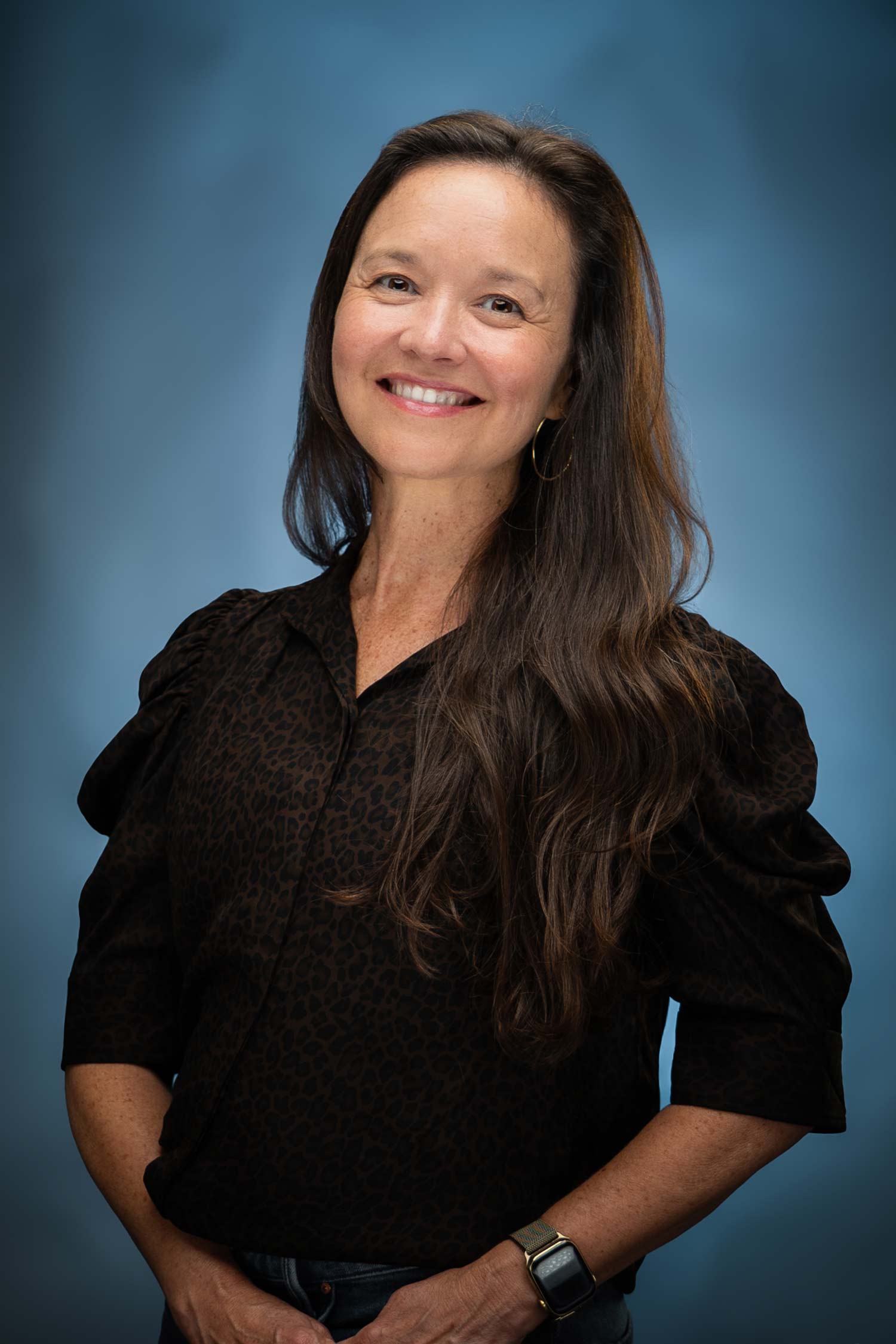 Smiling woman with long dark hair wearing a black blouse, photographed against a blue studio background.