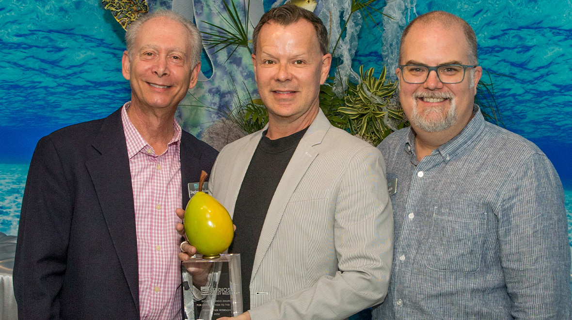 Three men smiling together at an event, with the man in the center holding a Golden Mango Award.