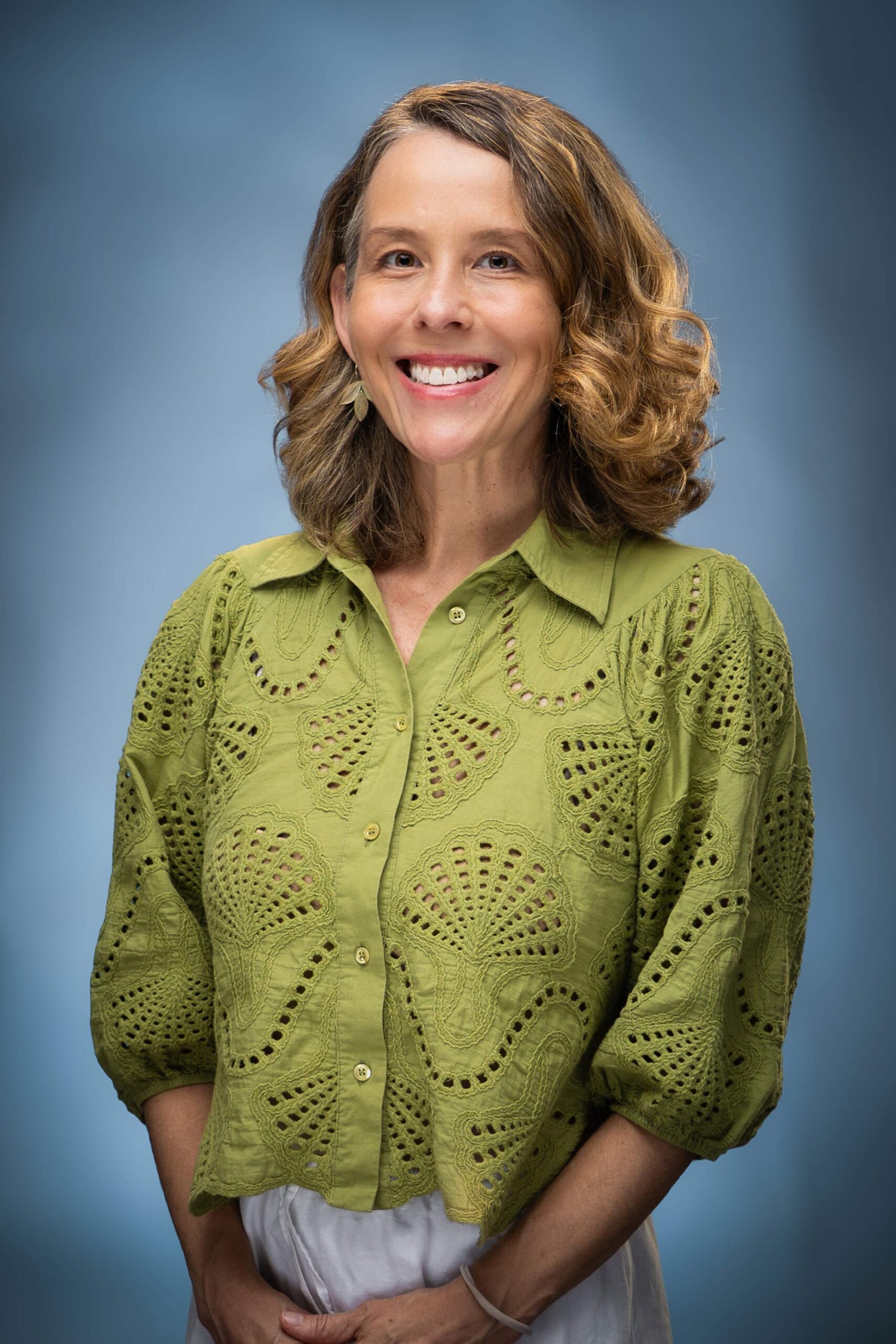 Headshot of Elena smiling in a green eyelet blouse against a blue studio background.