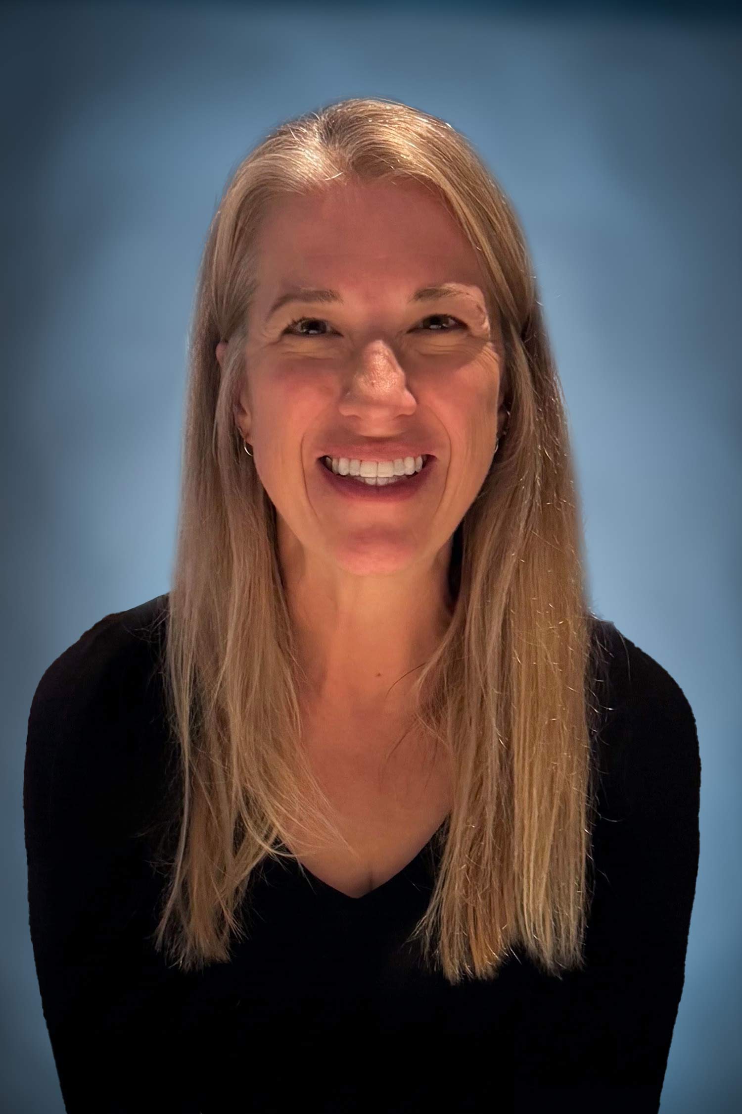 Portrait of Erin smiling against a blue background, wearing a black top with long blonde hair.
