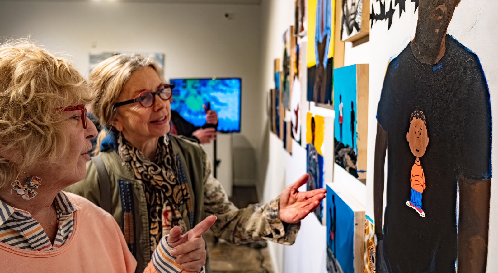 Two visitors discuss a colorful mixed-media artwork while exploring an exhibition at The Studios of Key West.