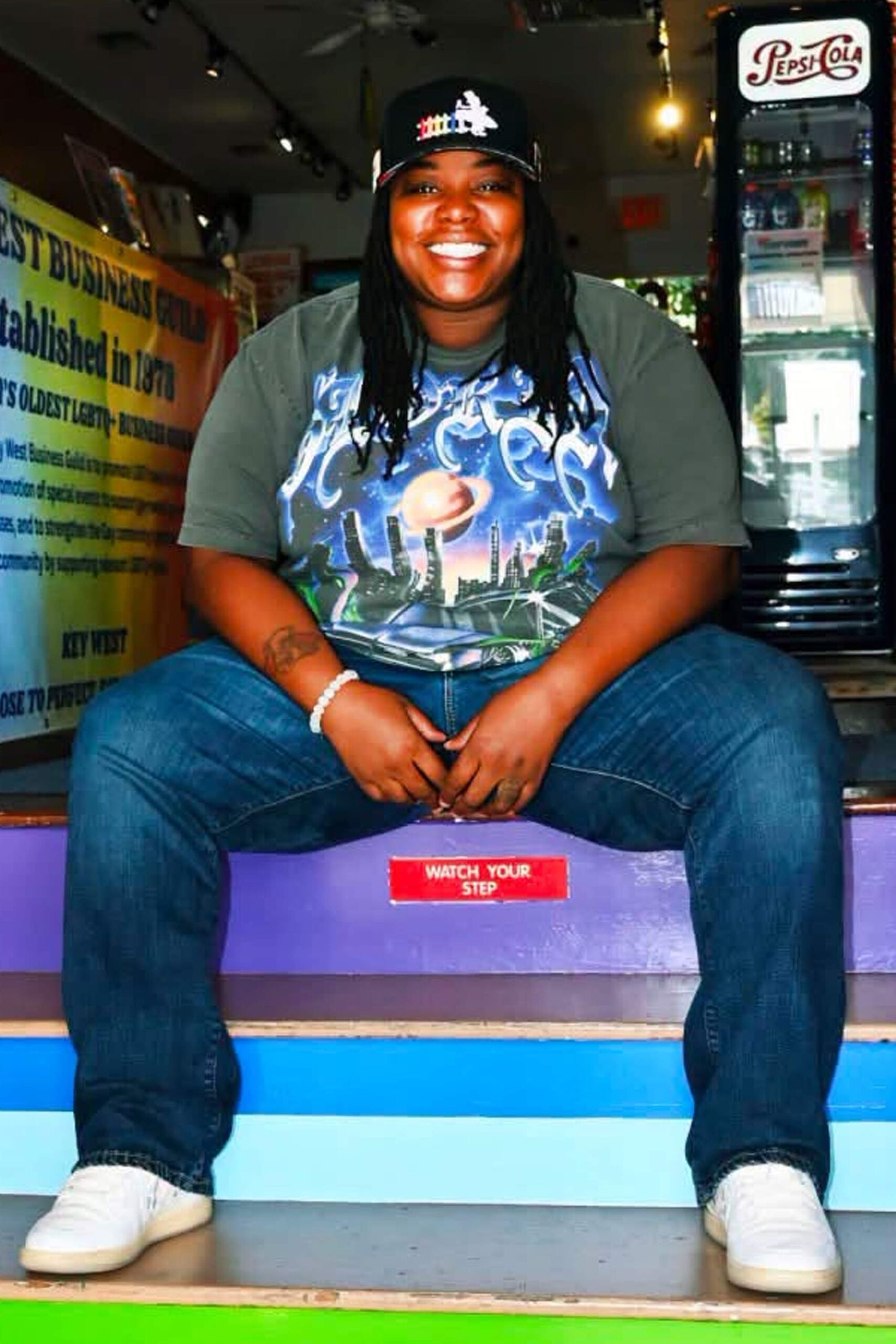 Headshot of Fritzie smiling while seated on colorful steps inside a Key West shop.