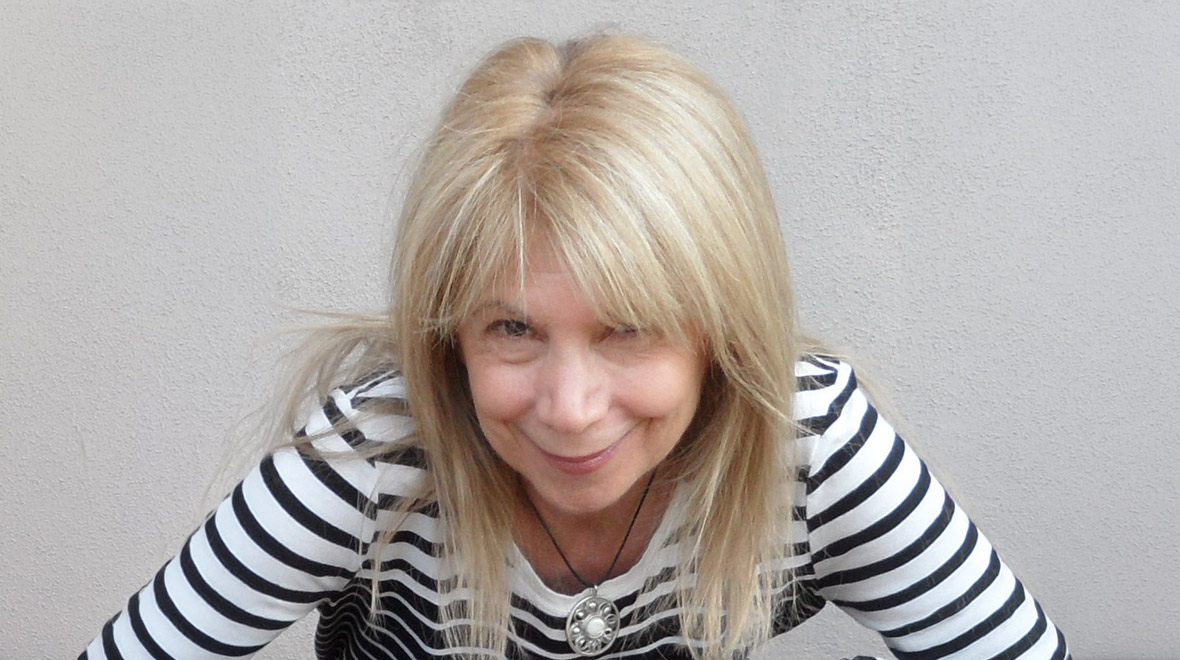 Portrait of Janice Gary smiling at the camera, wearing a black-and-white striped top against a light gray background.
