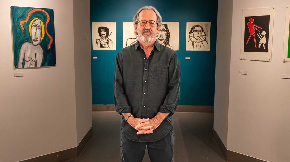 Man standing in an art gallery surrounded by colorful paintings and expressive figurative drawings.