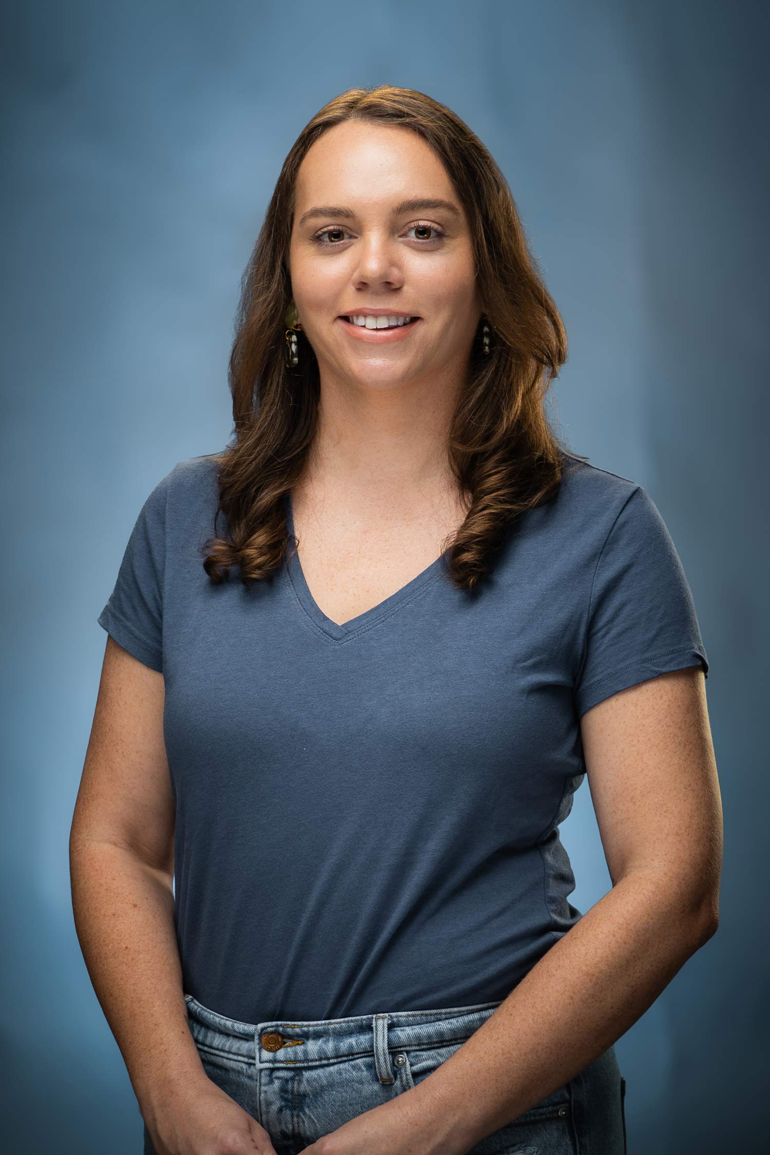 Headshot of Kalena smiling in a blue-gray top against a blue studio background.
