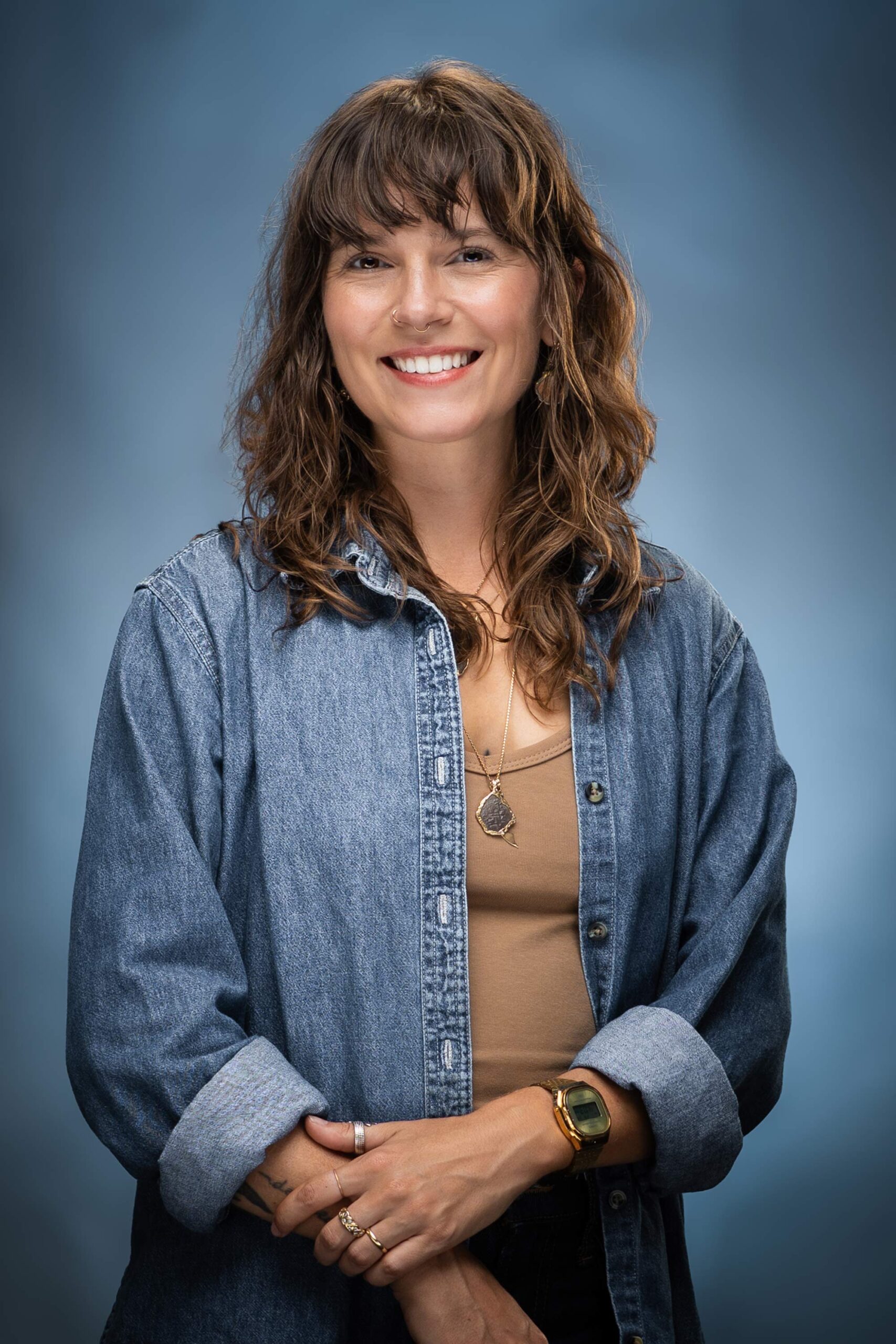 Portrait of Kota smiling in a denim shirt over a tan top against a blue studio background.