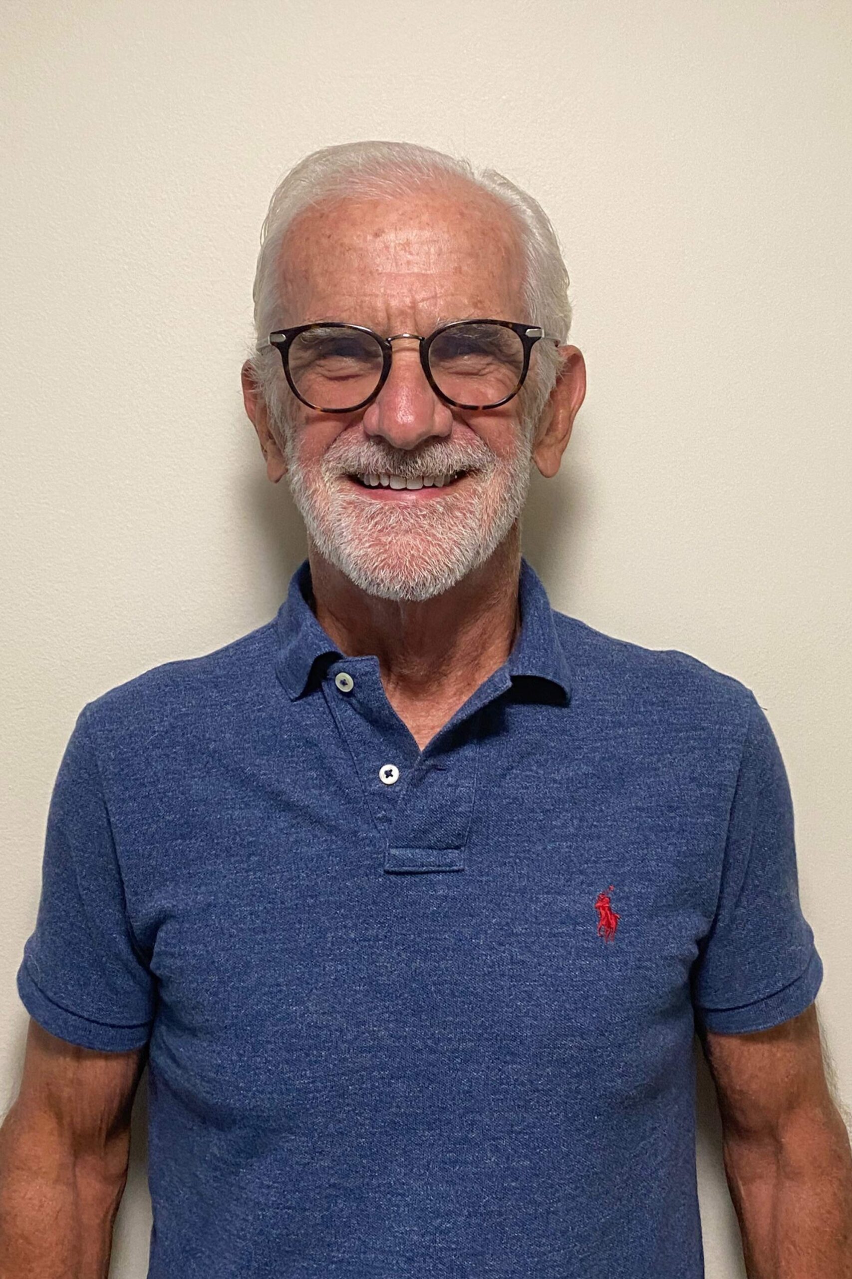 Man with glasses and a white beard smiling in a portrait.