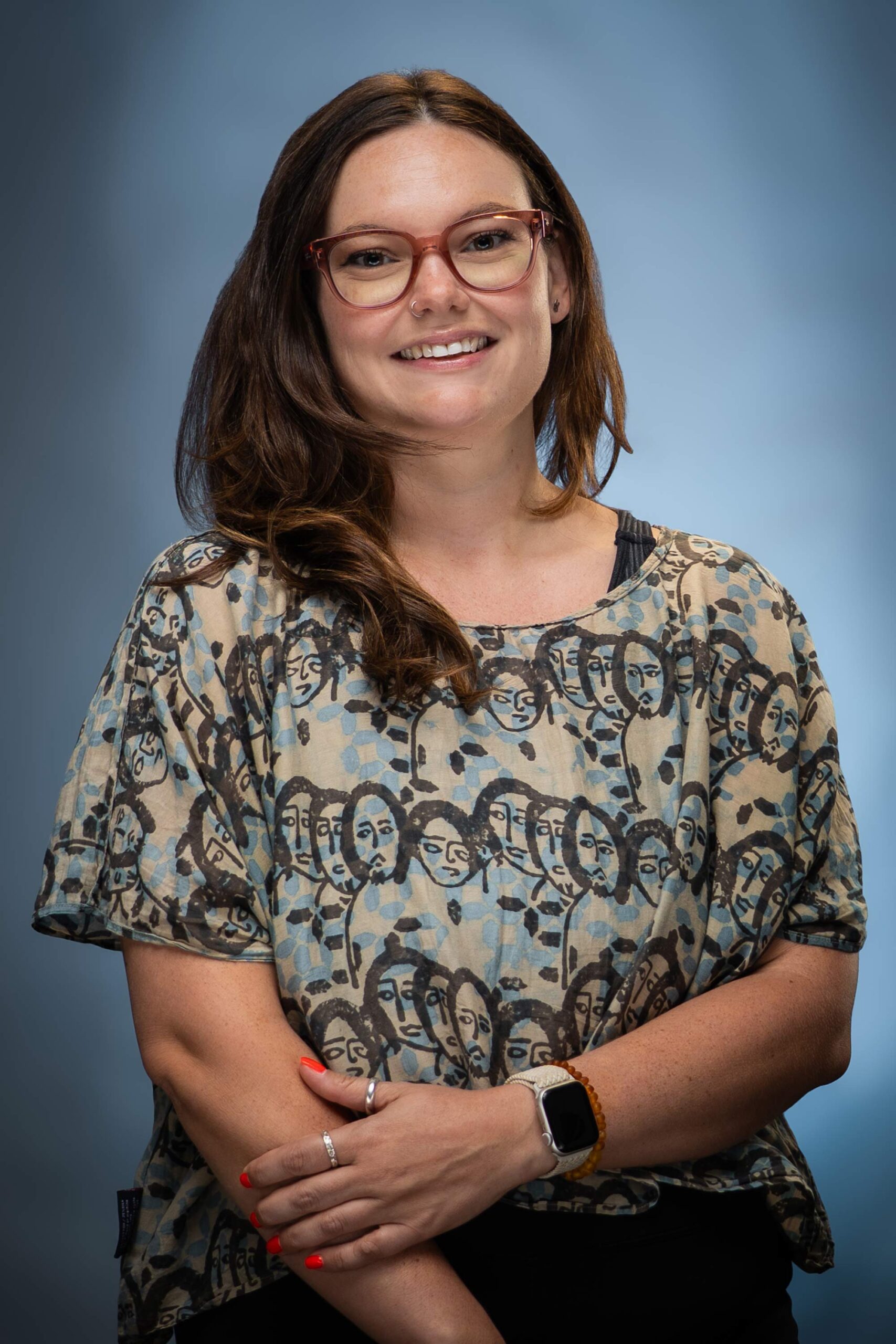 Headshot of Michelle Boscamp smiling at the camera, wearing glasses and a patterned top against a soft blue background.