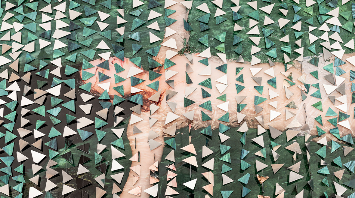 Reclining figure partially obscured by hundreds of layered green, white, and mirrored triangular shapes.