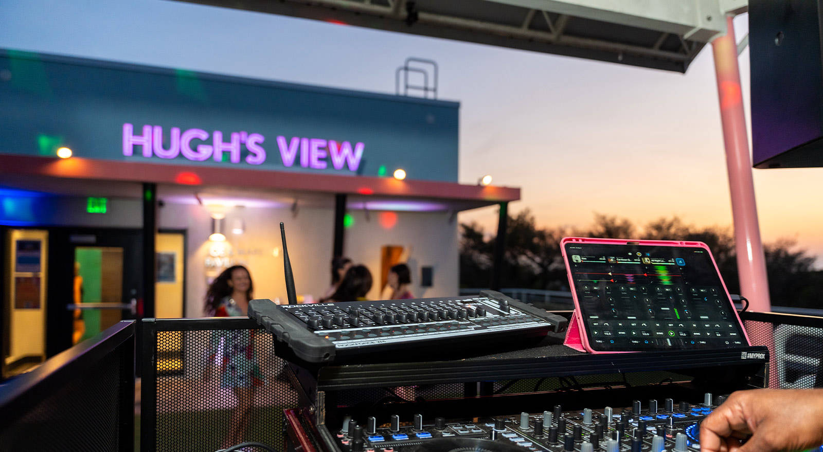 DJ equipment and mixing controls set up on Hugh’s View rooftop as guests gather during a private event at sunset.
