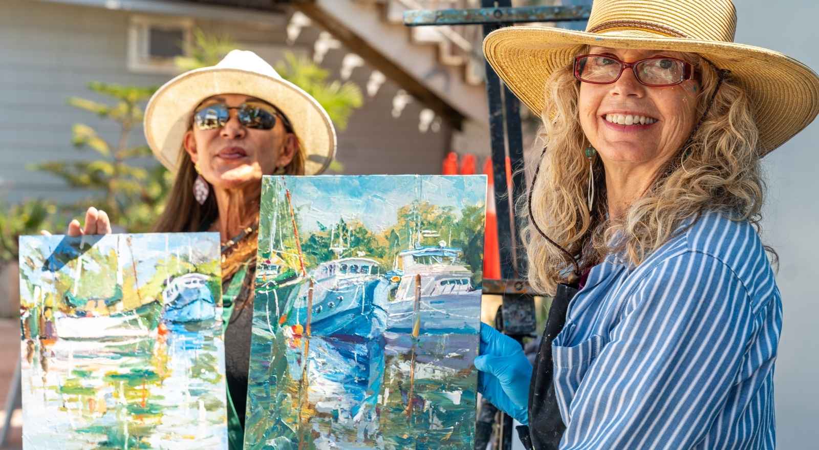 two artists holding paintings of boats