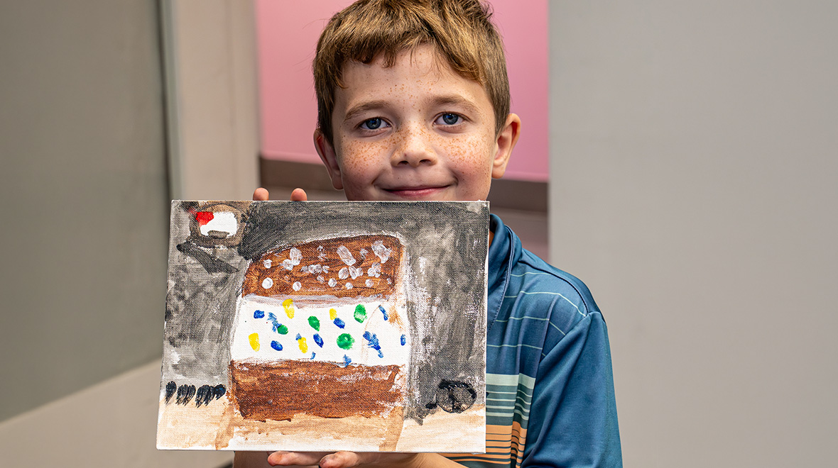 Smiling young student holds up his colorful painting on canvas during a Schools at The Studios art program.