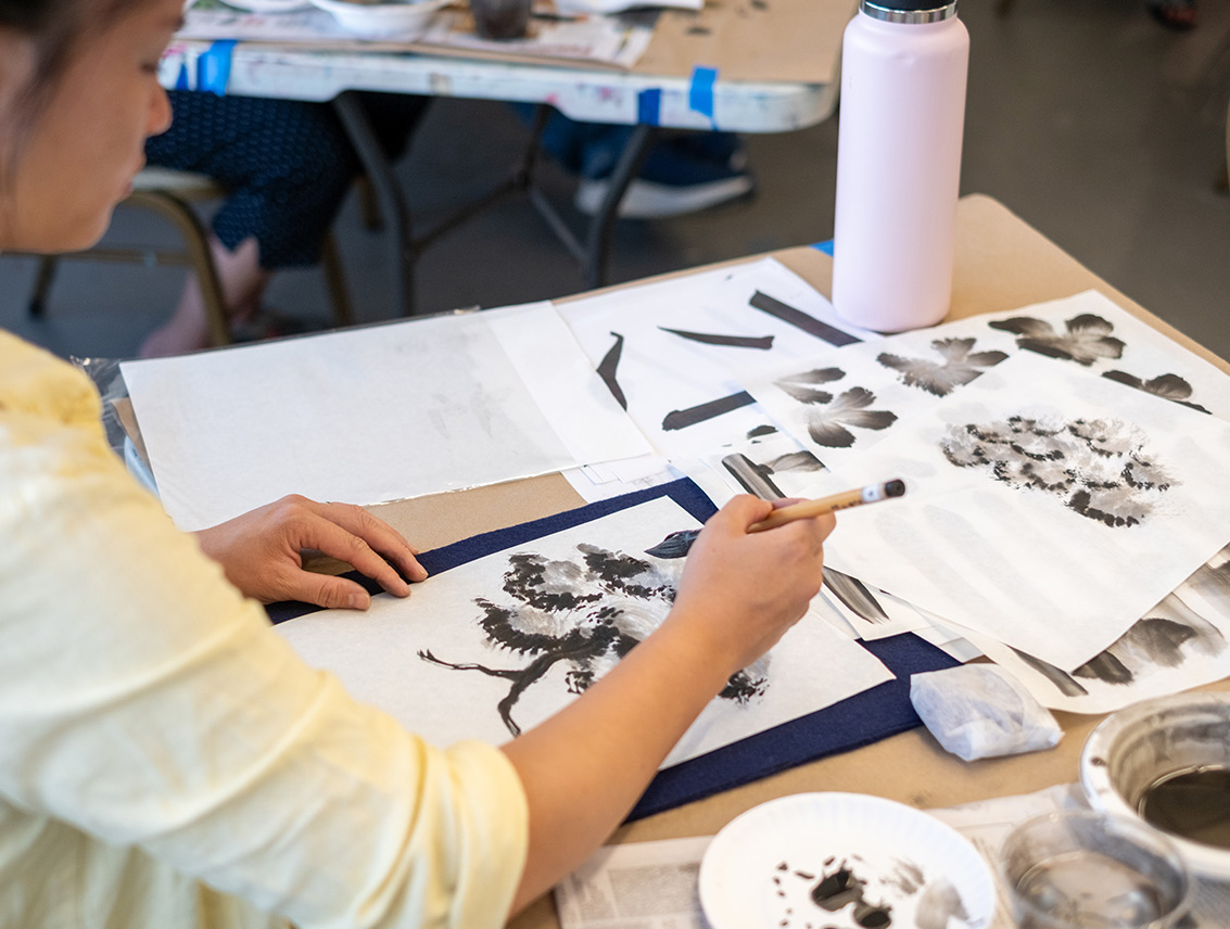 A student uses a brush and black ink to paint trees and botanical forms during a sumi-e painting class.