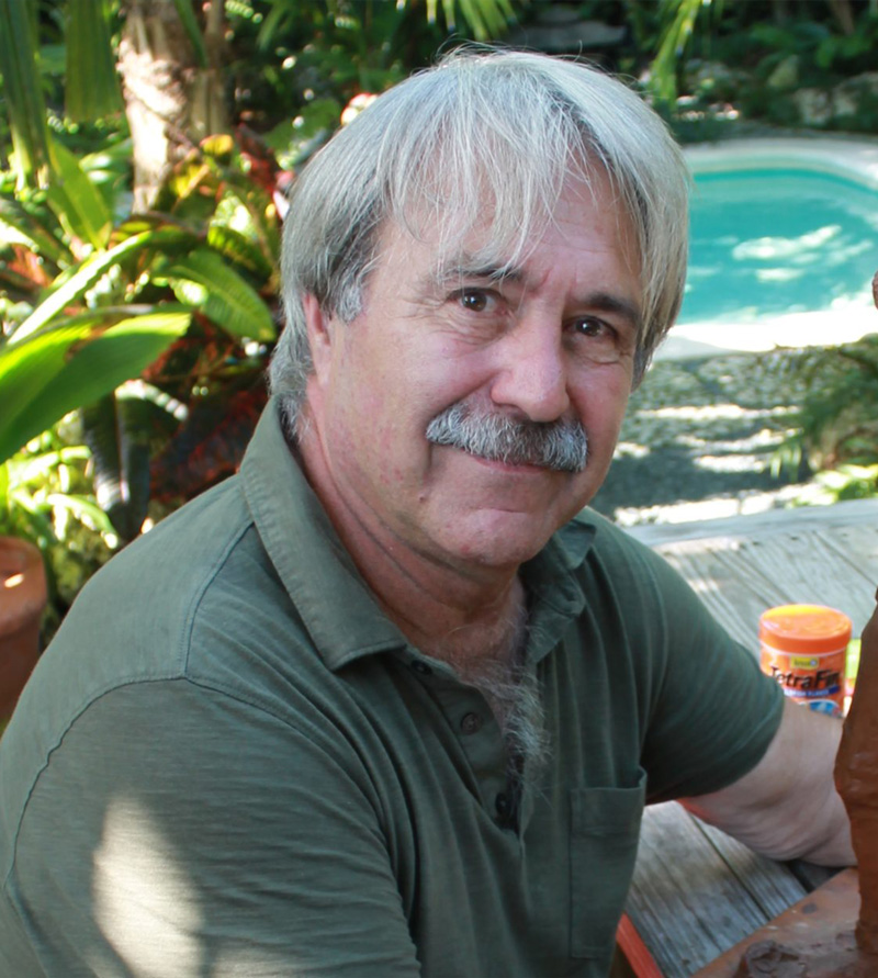 Tom Joris seated outdoors in a lush tropical garden.