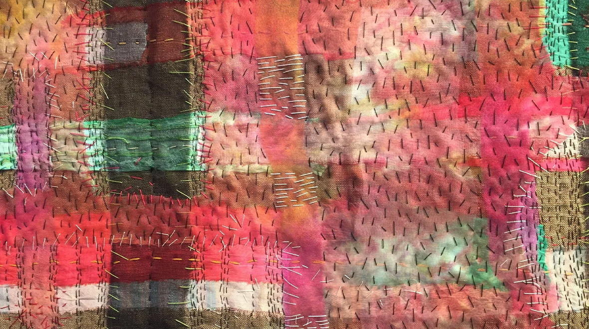 Close-up of layered, hand-stitched fabric in rich pink, red, green and brown tones, with visible contrasting threads and patchwork textures.