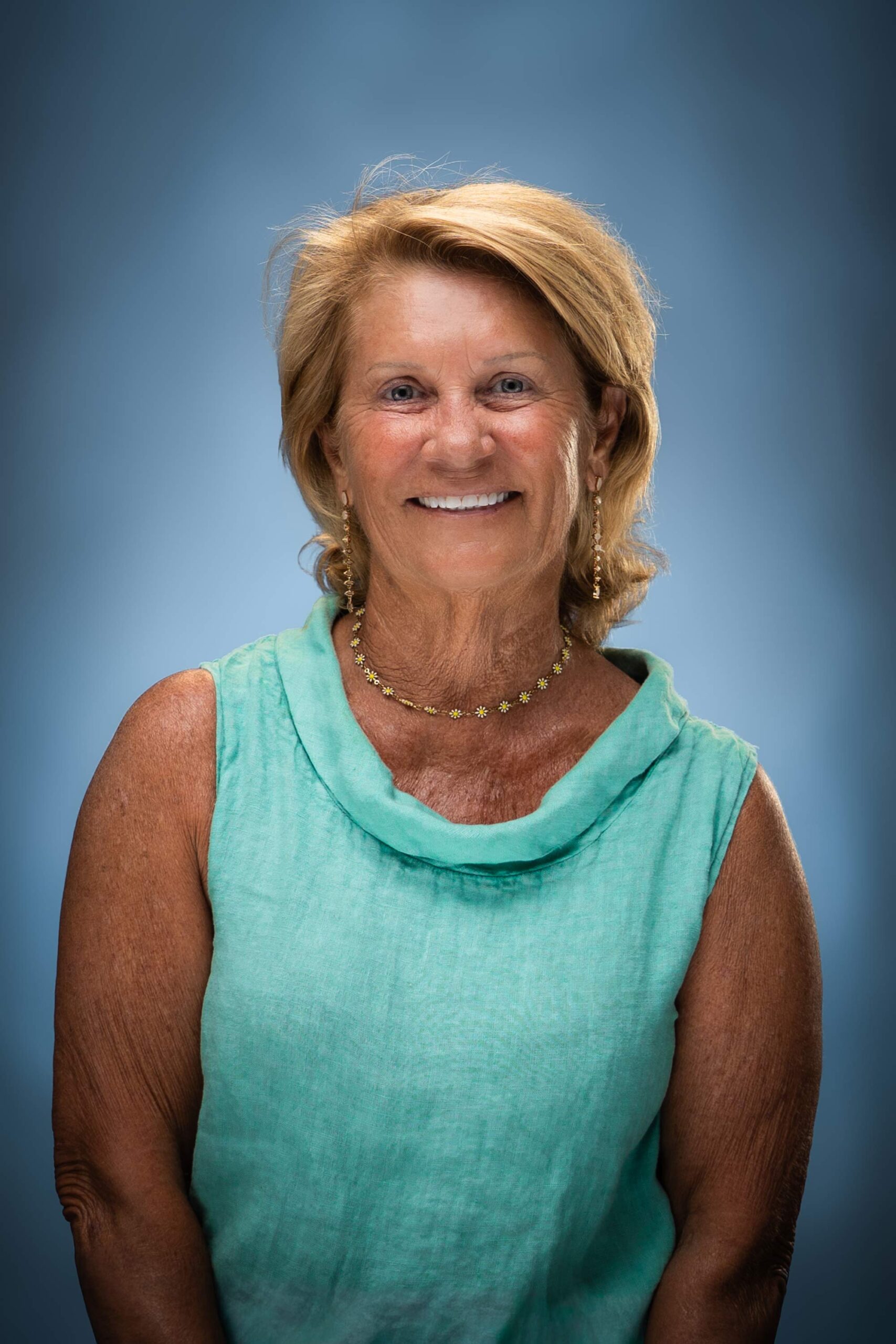 Headshot of Yolande smiling in a turquoise sleeveless top against a blue studio background.