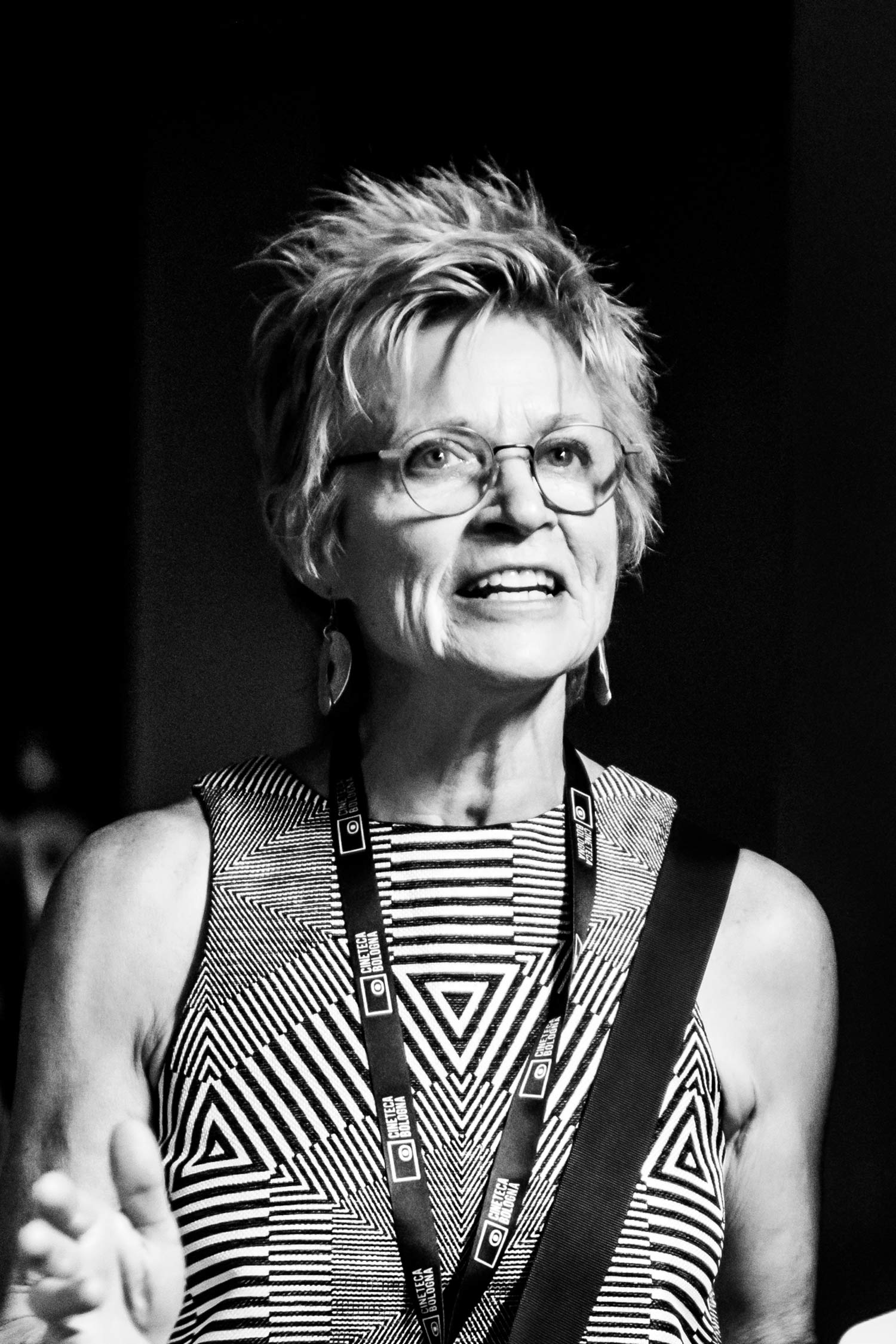 Black-and-white portrait of a smiling woman with short hair and round glasses, wearing a bold geometric patterned top.